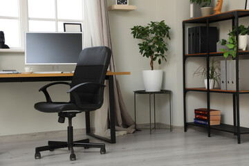 Interior of office with desk, black chair and shelf unit