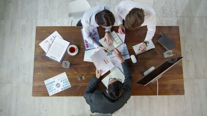 High-angle, top-down view of a professional business team collaborating around a wooden desk,...