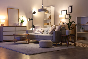 Interior of living room with sofa, shelf unit and glowing lamps in evening