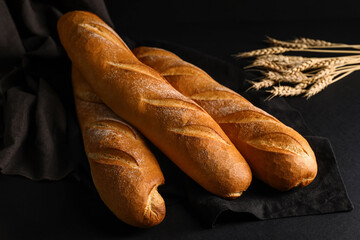 Fresh baguettes and wheat on black background