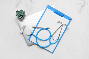 Laptop with flash drive, clipboard and medical stethoscope on white grunge background