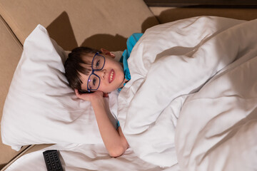 Boy with glasses lying in bedroom on bed and smiling