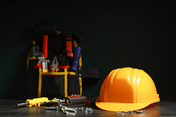 Bag with construction tools and hardhat on black background