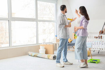Young pregnant couple with paint roller during repair in children's room