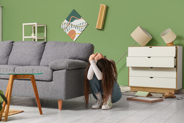 Scared young woman covering head near sofa in living room during earthquake
