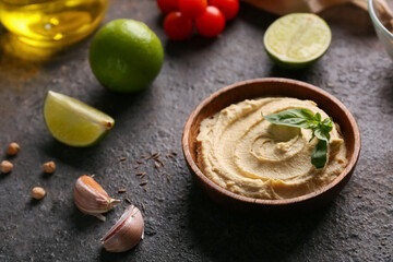 Bowl of tasty hummus with ingredients on black grunge background, closeup