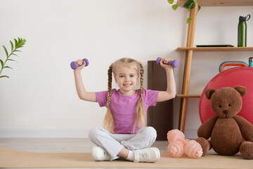 Sporty little girl with dumbbells training on mat at gym