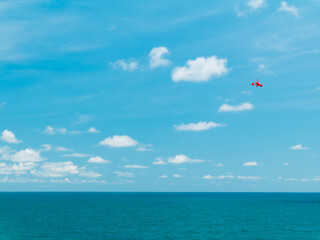 Red Helicopter flies near the beach blue skies and clouds on a perfect summer day over the water