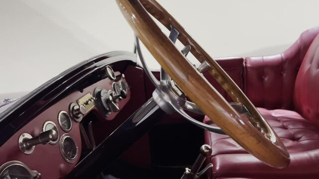 Close-up view of a vintage car interior featuring a polished wooden steering wheel, classic chrome details, and burgundy leather seats. 
