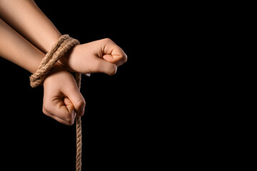 Hands tied together with rope on black background. Concept of oppression