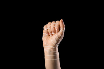 Hand with clenched fist wrapped with string on black background. Concept of oppression