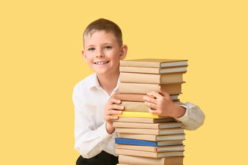 Smiling little boy with stack of books against color background