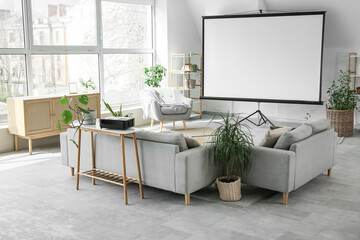Interior of light room with blank projector screen, sofas and plants