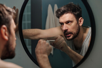 Caucasian young adult man standing in front of mirror pointing finger at own reflection with...