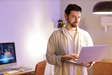 Handsome man working with laptop at office in evening