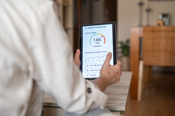 Woman sitting on a sofa is using a tablet showing an energy monitoring app, checking current usage, weekly trends, and smart scheduling options to optimize energy consumption in her home