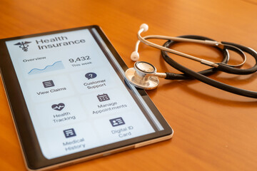 Tablet displaying health insurance application with stethoscope lying on wooden table representing healthcare technology and online medical services