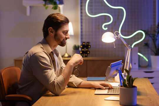 Handsome young man working with laptop in office at night - Powered by Adobe