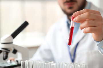 Male scientist with test tube and microscope in laboratory, closeup