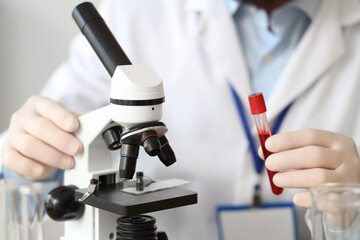 Male scientist with test tube and microscope working in laboratory, closeup