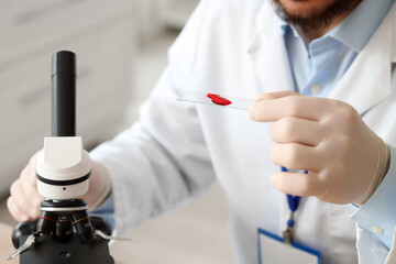 Male scientist with blood sample and microscope in laboratory, closeup