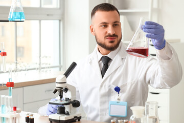 Male scientist with flask and microscope working in laboratory
