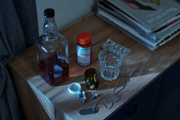 Close-up showing glass bottle of alcohol, prescription pill bottles, scattered pills, glass of...