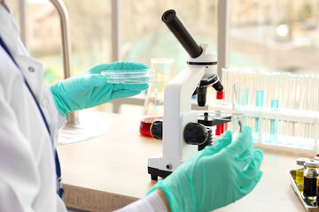 Female scientist with microscope and Petri dish in laboratory, closeup