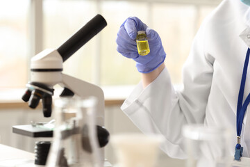 Female scientist with ampule and microscope at table in laboratory, closeup