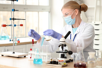 Fototapeta premium Female scientist with test tubes and microscope working in laboratory
