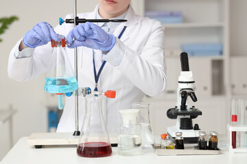 Female scientist with flask on stand and microscope working in laboratory