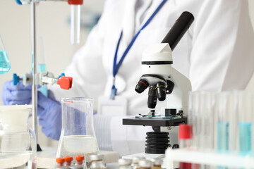 Microscope on table against female scientist working in laboratory, closeup