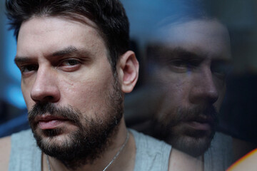 Portrait of Caucasian man looking into camera with serious expression, face partially reflected in...
