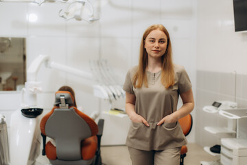 Dentist posing in her office with patient waiting in background