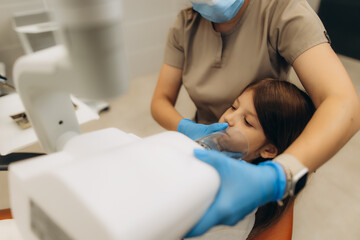 Dentist holding anesthesia mask on girl's face in dental clinic