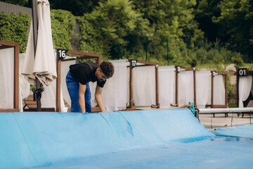 Pool maintenance worker covering swimming pool with blue tarp at resort