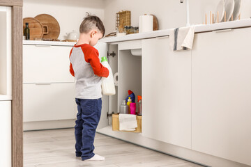 Little boy with detergent near open drawer in kitchen, back view. Child at risk