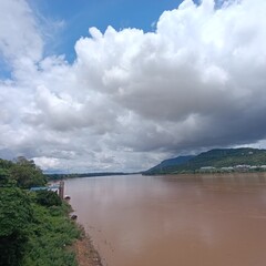 A panoramic view of the wide Mekong River flowing past the lush green riverbanks of Pakse, Laos  -...