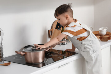 Little boy touching cooking pot on stove in kitchen. Child at risk