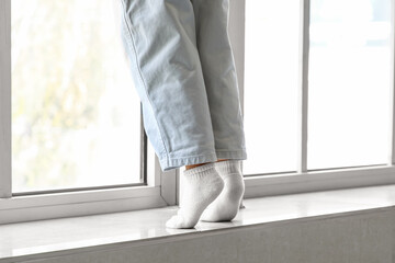 Little boy on windowsill at home, back view. Child in danger