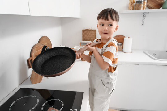 Little boy taking frying pan from stove in kitchen. Child at risk