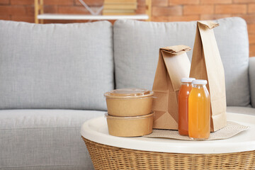Paper bags with containers and juice on table in living room, closeup. Food delivery service