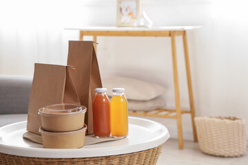 Paper bags with containers and juice on table in living room, closeup. Food delivery service