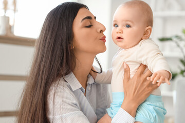 Beautiful young happy mother kissing her cute little daughter at home