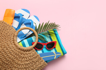 Wicker bag with beach accessories and bottle of sunscreen cream on pink background, closeup