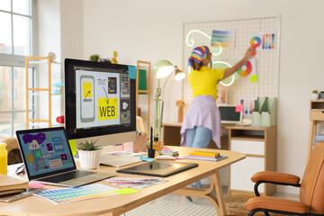 Workplace with computer and laptop against female web designer working in office