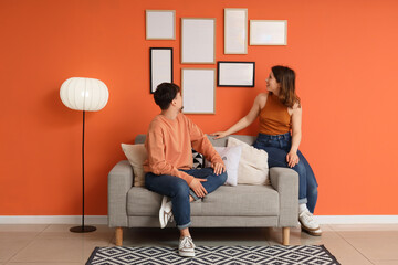 Young couple sitting on sofa near hanging blank frames at home