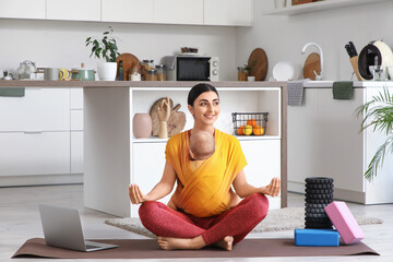 Sporty young woman with her baby in sling meditating at home