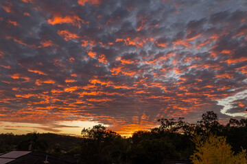 A dramatic sunrise lights up the clouds in bright orange color, adding a few sunrays to complete...