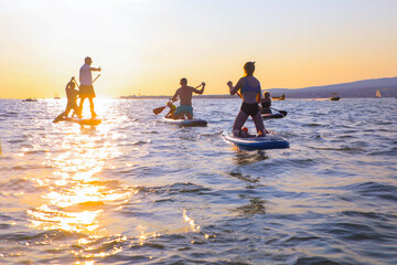 young people  riding  on sup surfing in the sea at sunset
